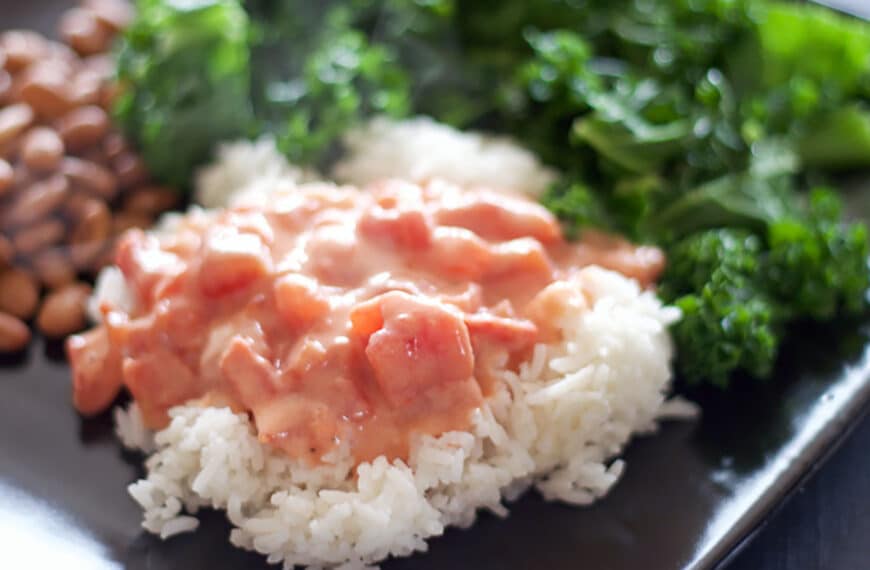 tomato gravy over white rice in the foreground on a black plate in the background on the left are pinto beans and on the right is sautéed greens