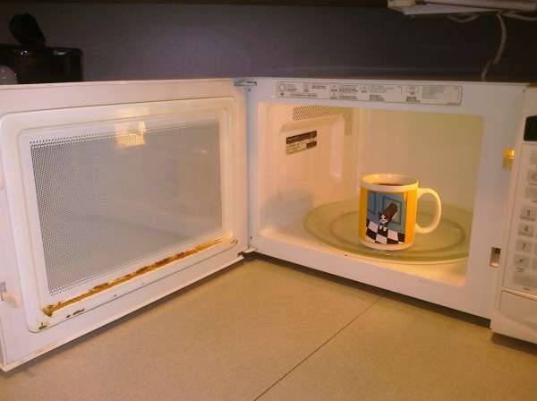 open rusty microwave with a mug