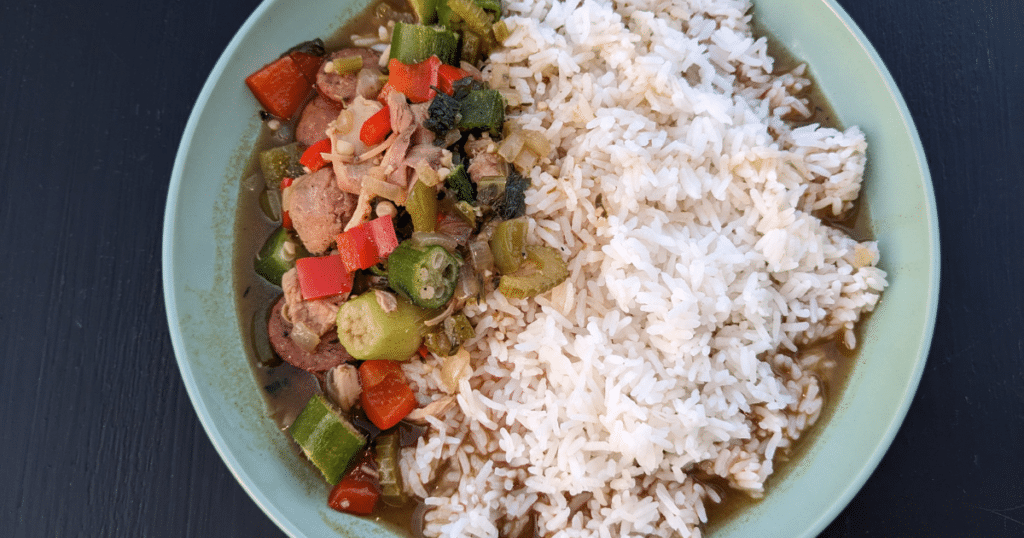 chicken gumbo and white rice in a pale green bowl on a black background